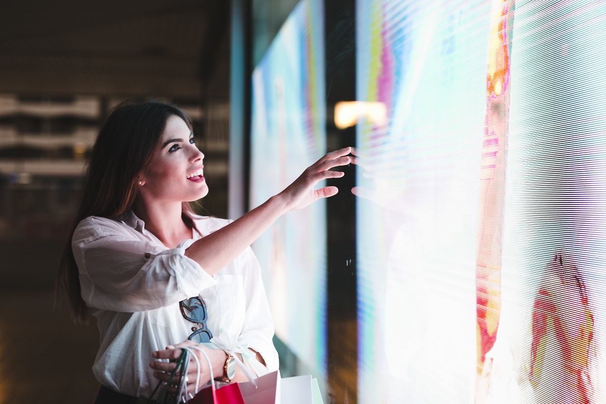 woman holding shopping bags looking at a digital signage display