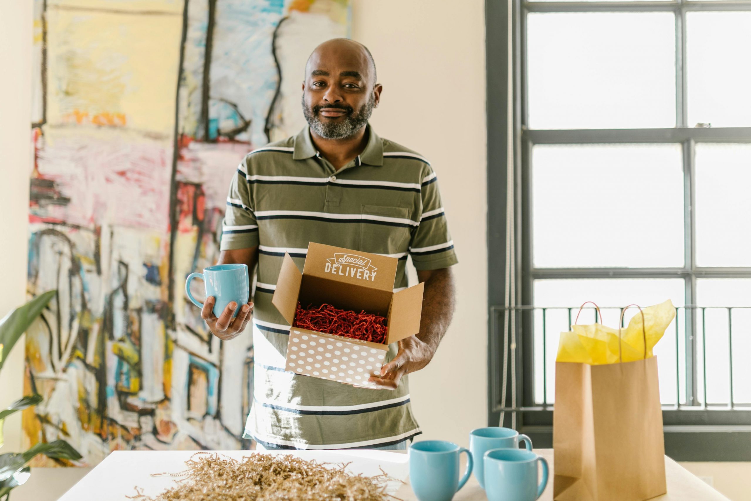small business owner holding a blue ceramic cup on one hand and a special delivery box on the other